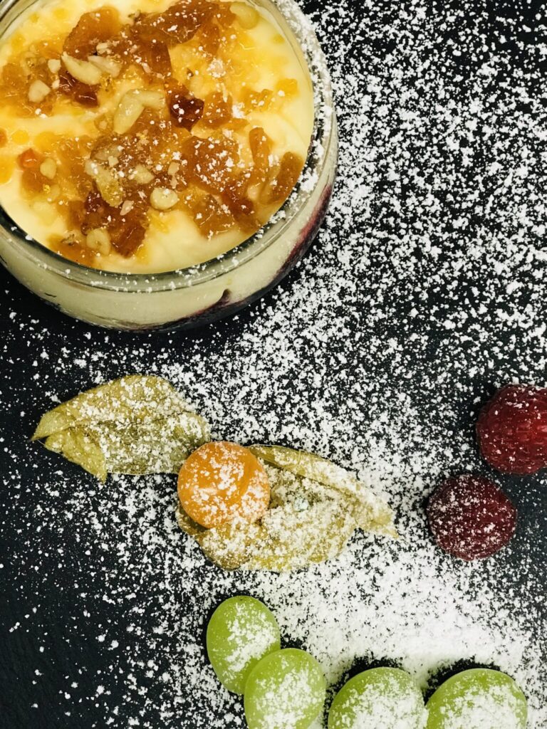 Dessert im Glas mit karamellisierten Nüssen und frischen Früchten auf Puderzucker-Dekor.