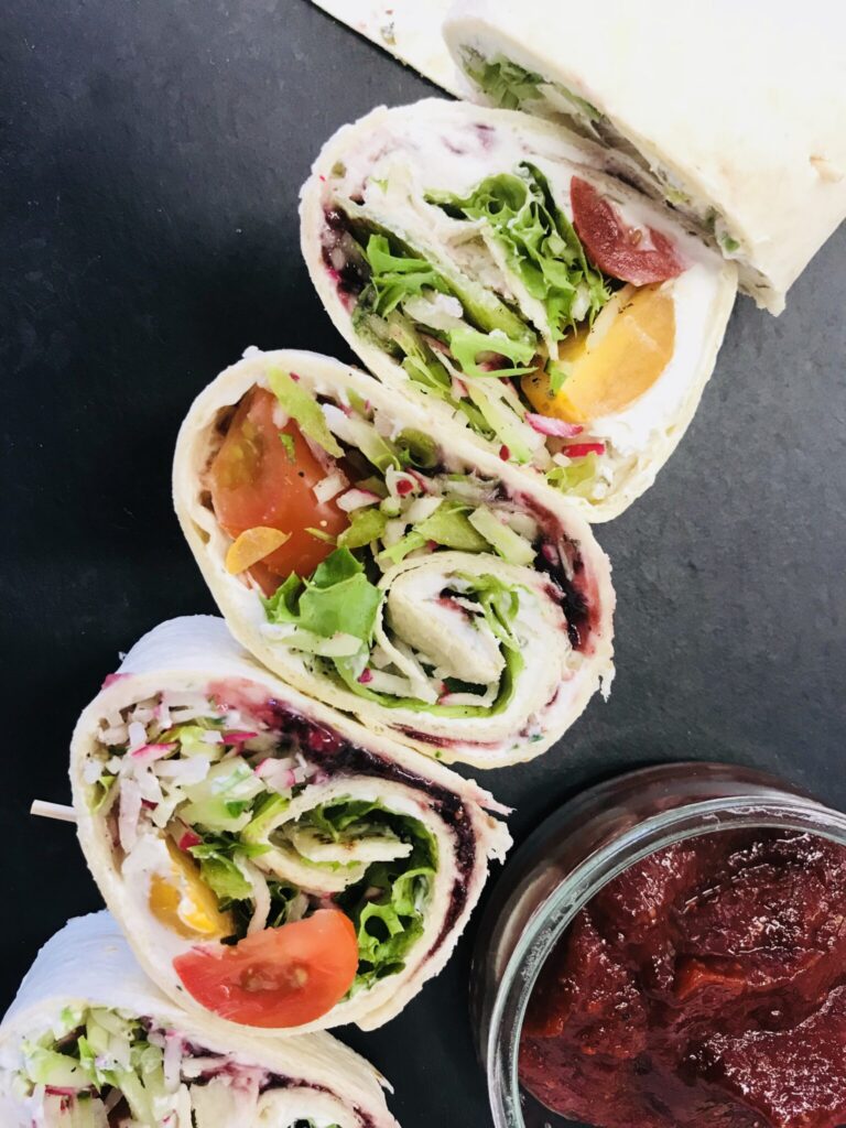 Wrap-Rollen mit frischem Gemüse und Dip auf einer schwarzen Platte.